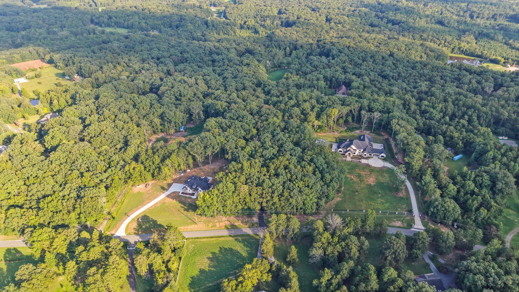 Aerial view of the clearing, the residence and the drive within surrounding woodland