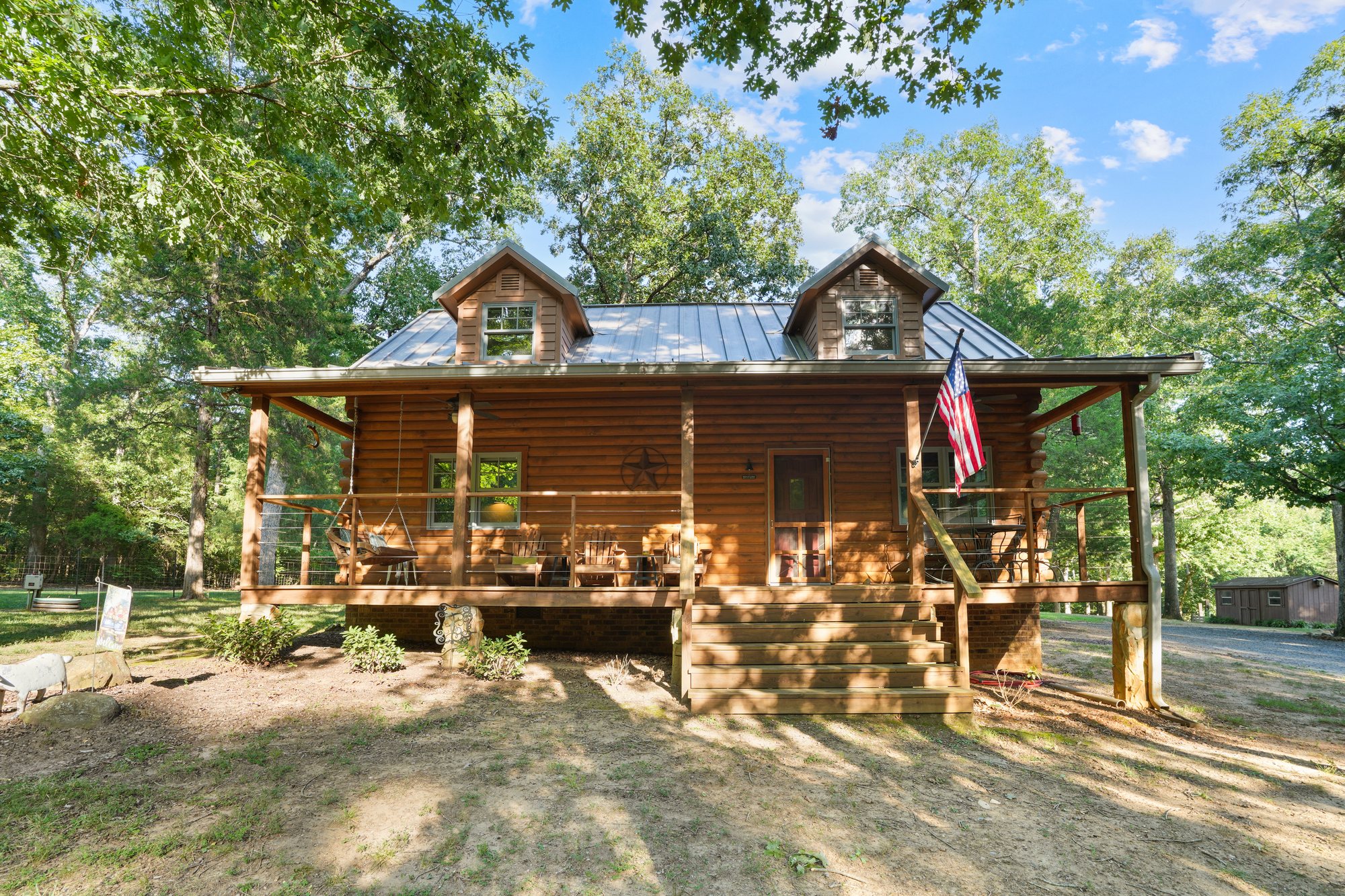 The log residence with its covered porch, set among mature trees at the end of the drive