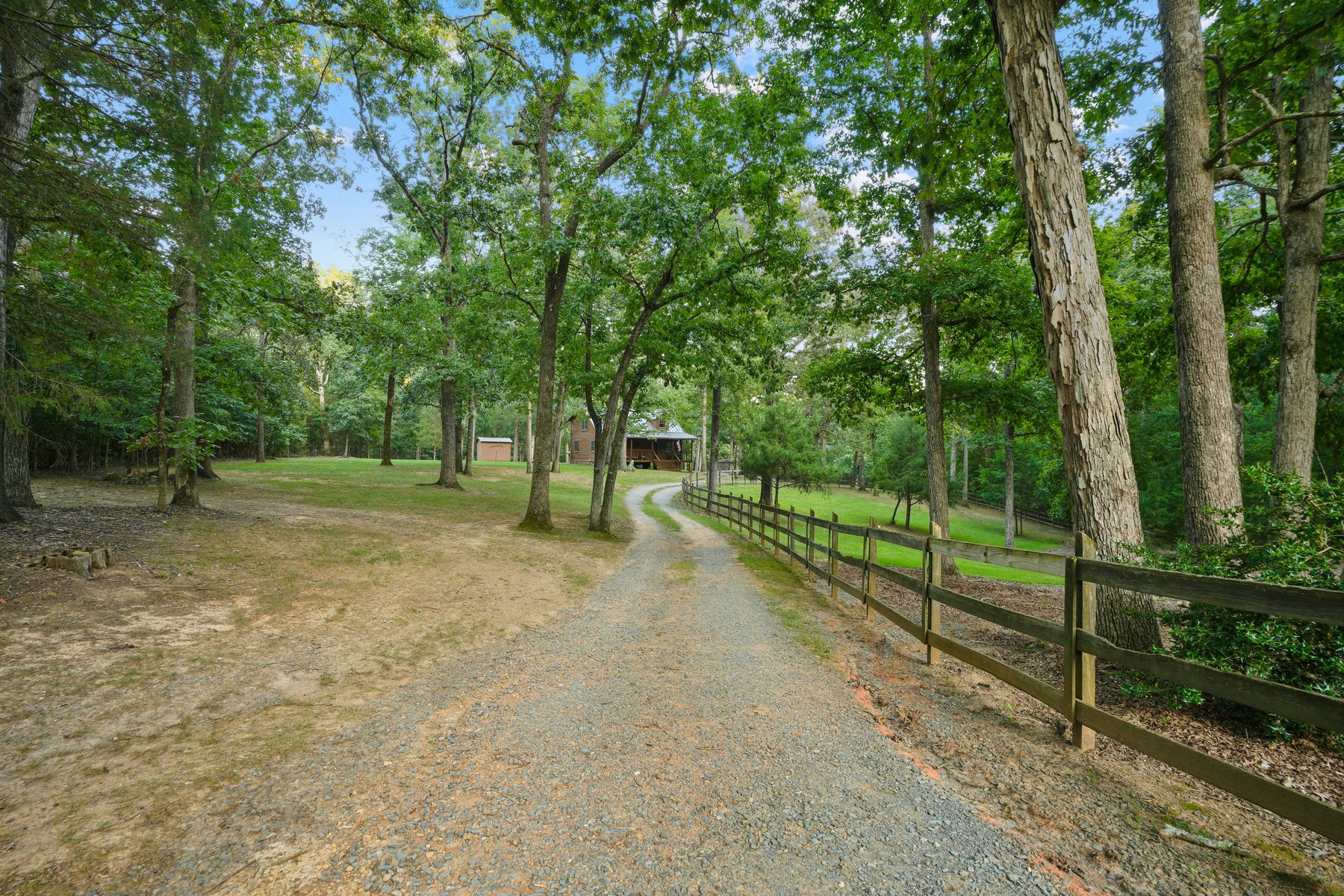 The gravel entrance drive running between rail fencing under mature trees