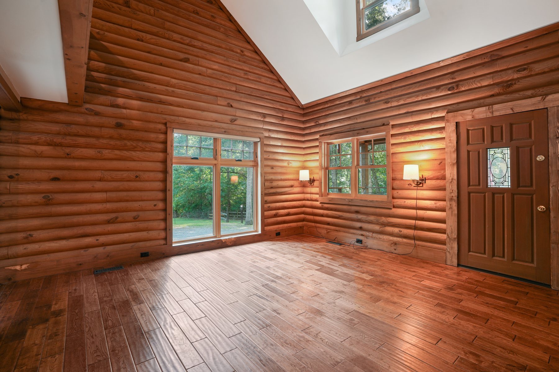 The great room with log walls, hardwood floors and windows to the trees